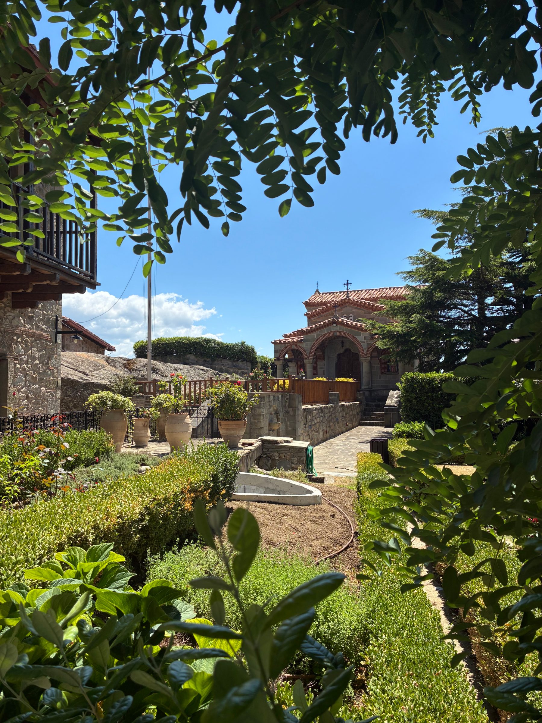 A monastery courtyard garden with planted urns, a small chapel and a cypress tree.